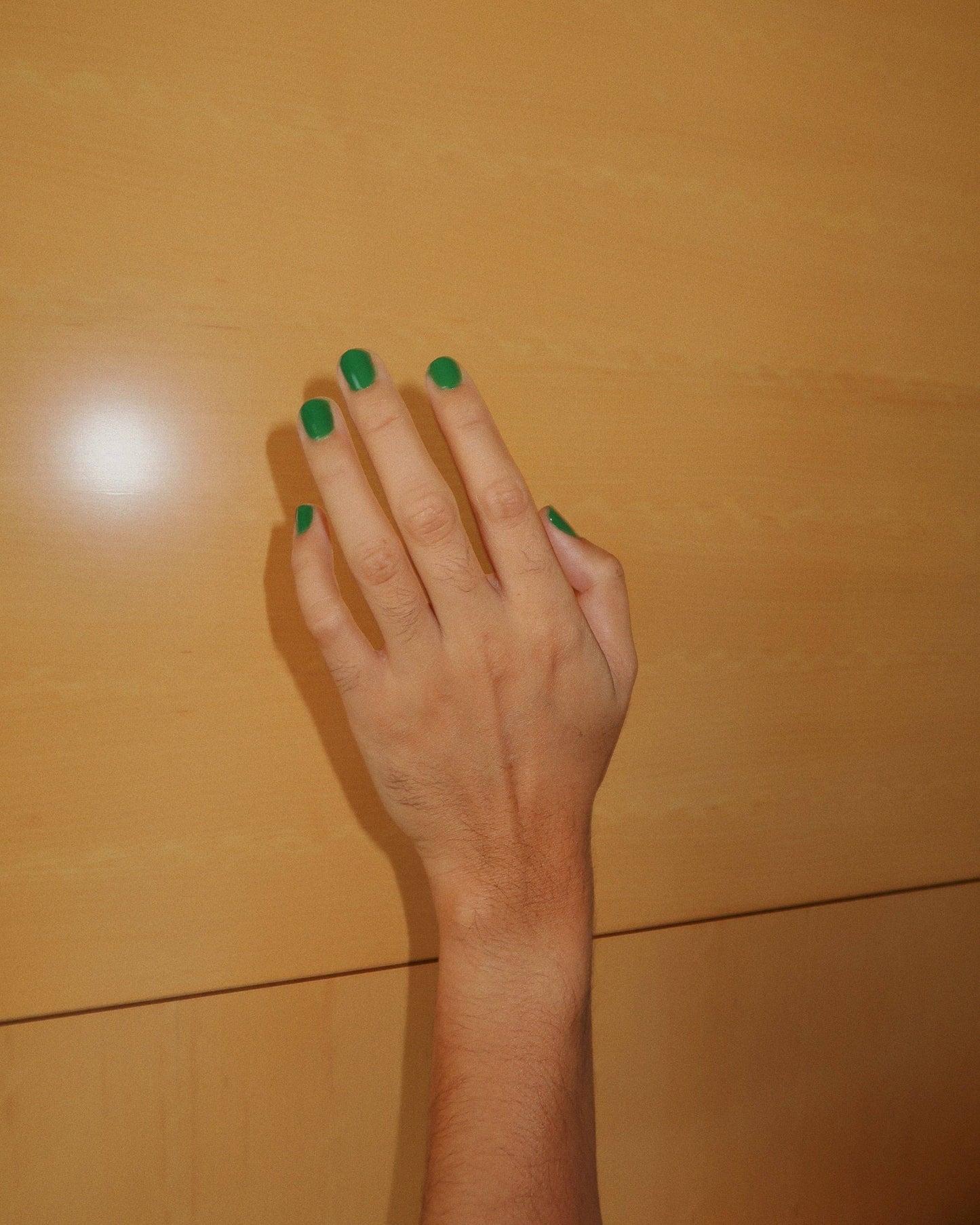 Hand with green nail polish on a wooden surface, Maryjane Medium Green Nail Polish Ruth POlish