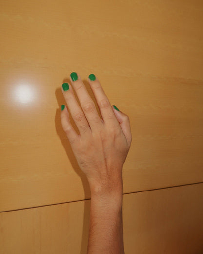 Hand with green nail polish on a wooden surface, Maryjane Medium Green Nail Polish Ruth POlish