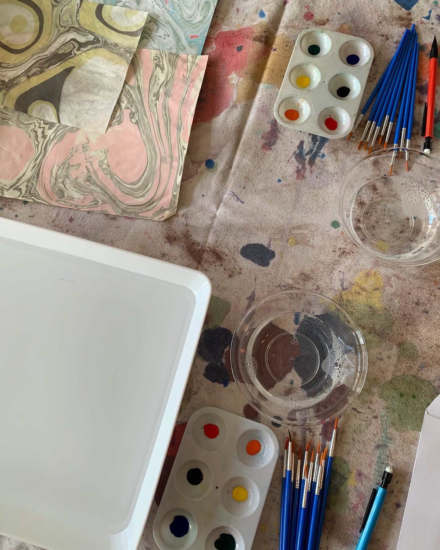 Artistic workspace with paintbrushes, color palettes, and a canvas on a textured surface.
