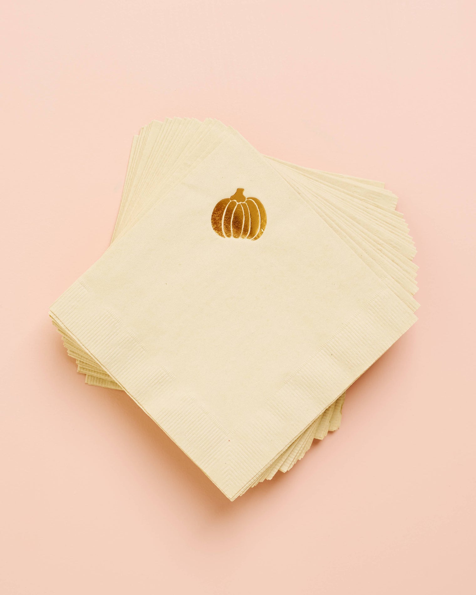 Stack of light green napkins with gold pumpkin design on a pink background