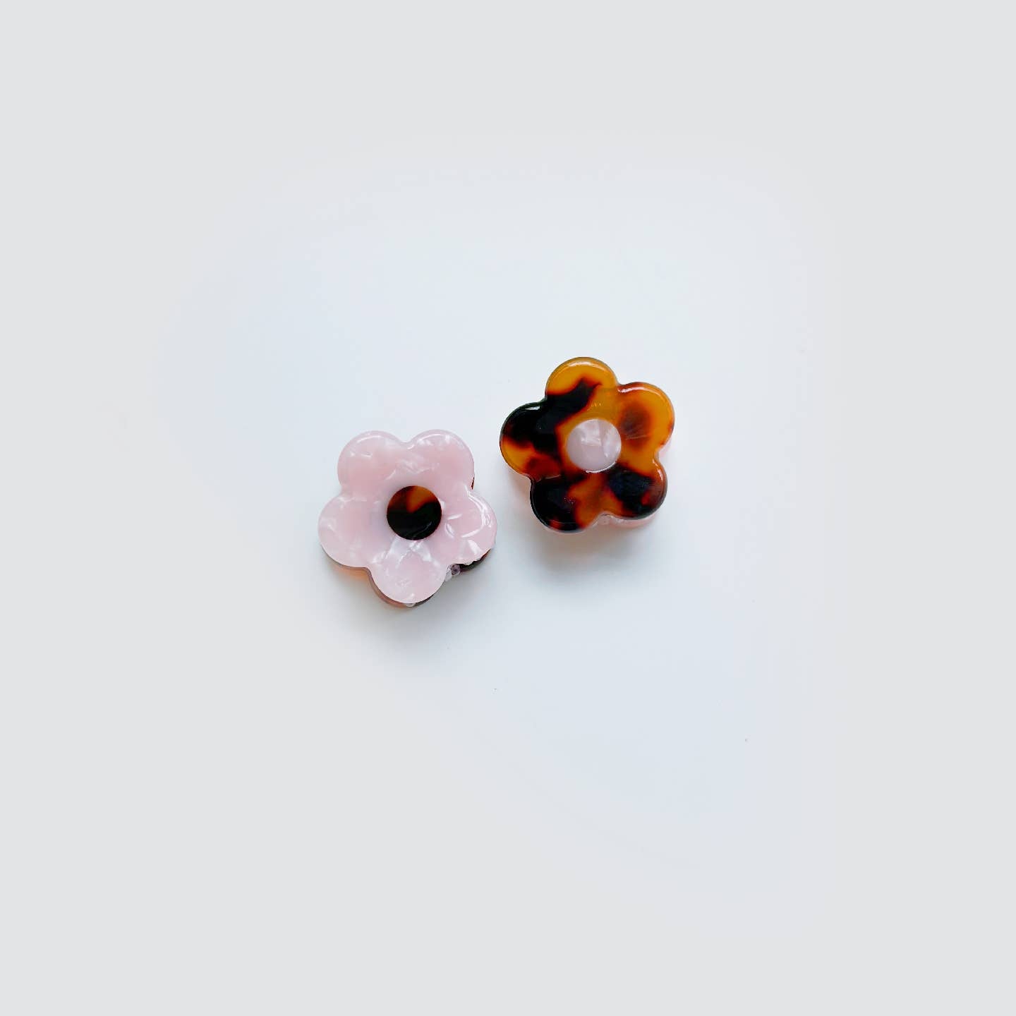 Two flower-shaped earrings, one pink and one tortoiseshell, on a light gray background.