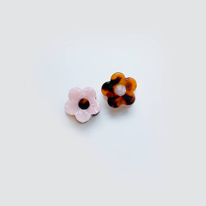 Two flower-shaped earrings, one pink and one tortoiseshell, on a light gray background.