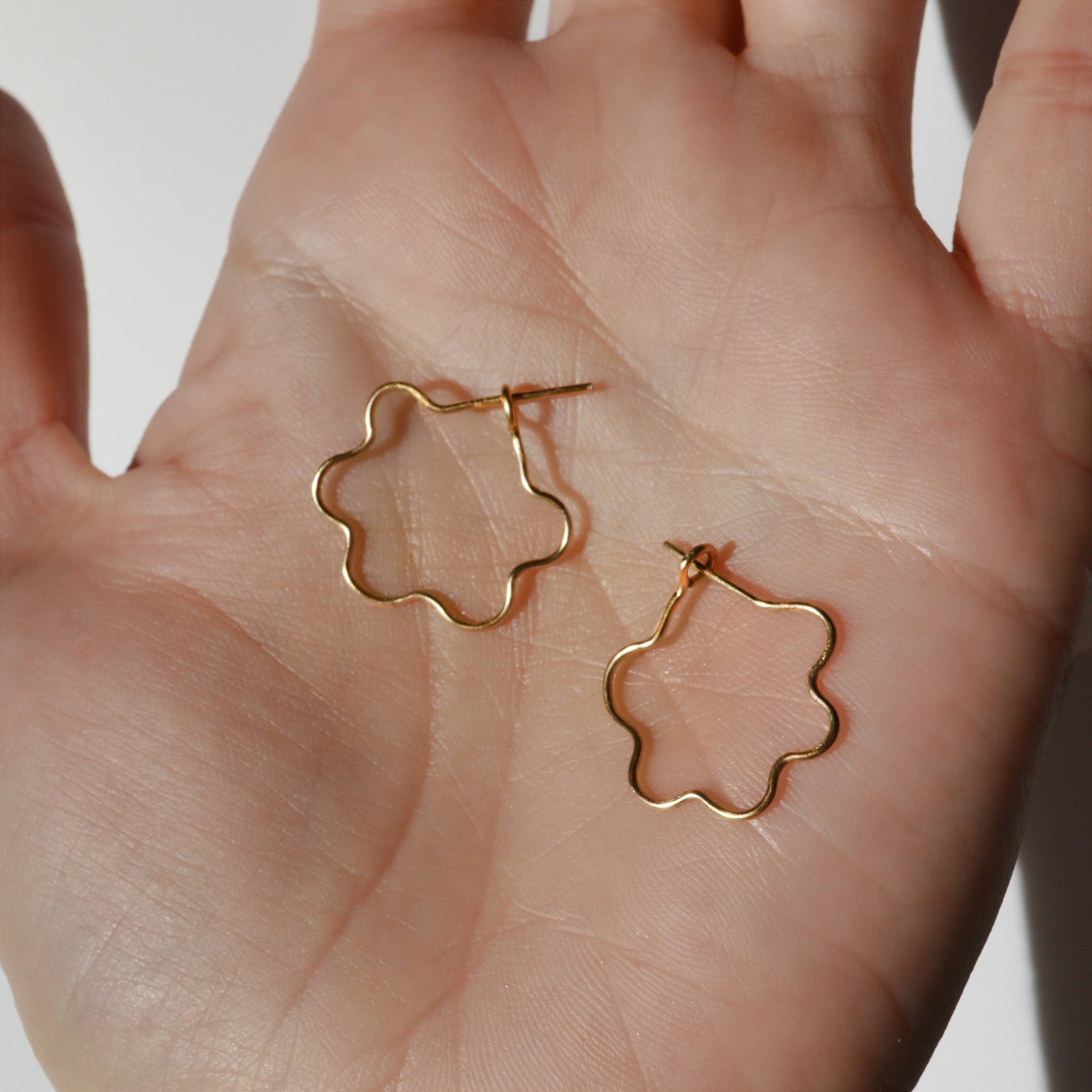 Gold flower-shaped earrings held in a hand against a neutral background, Mini Flora Hoop Earrings in Gold 