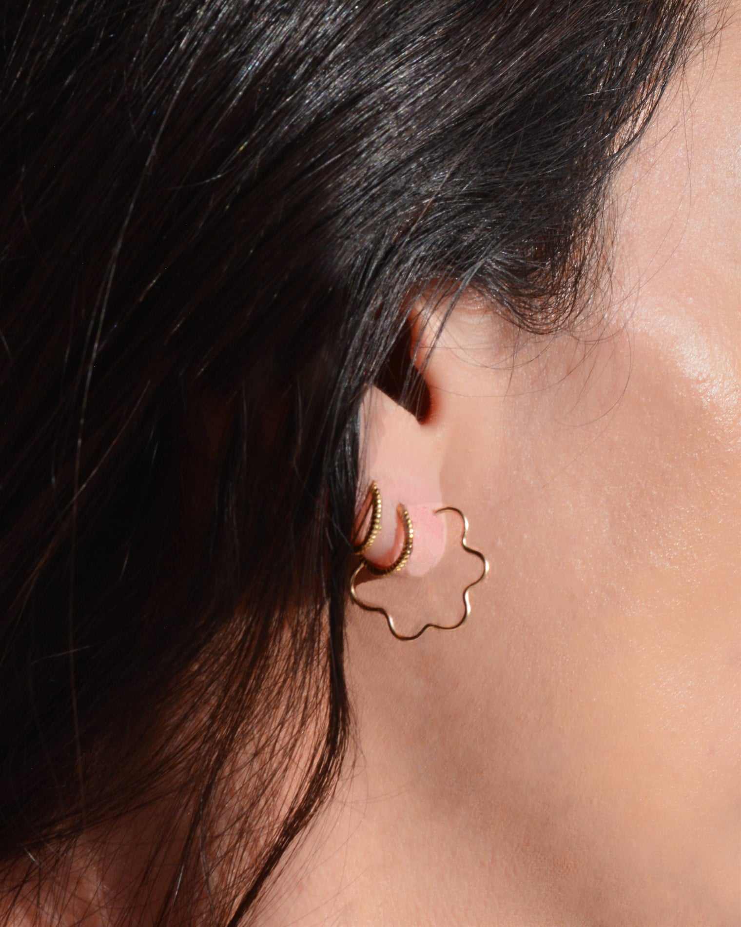 Close-up of a person wearing a gold flower-shaped earring.