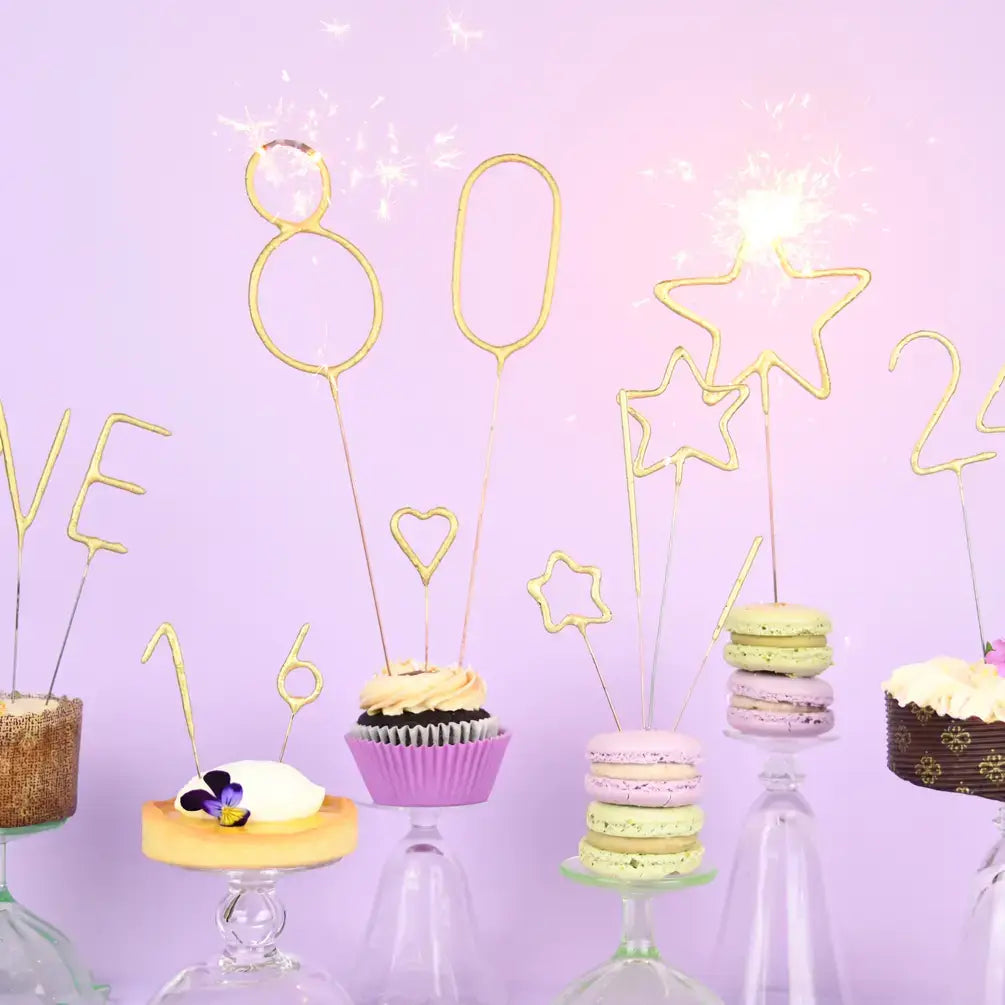 Decorative cake toppers shaped like stars, hearts, and numbers on a purple background with cupcakes and macarons.