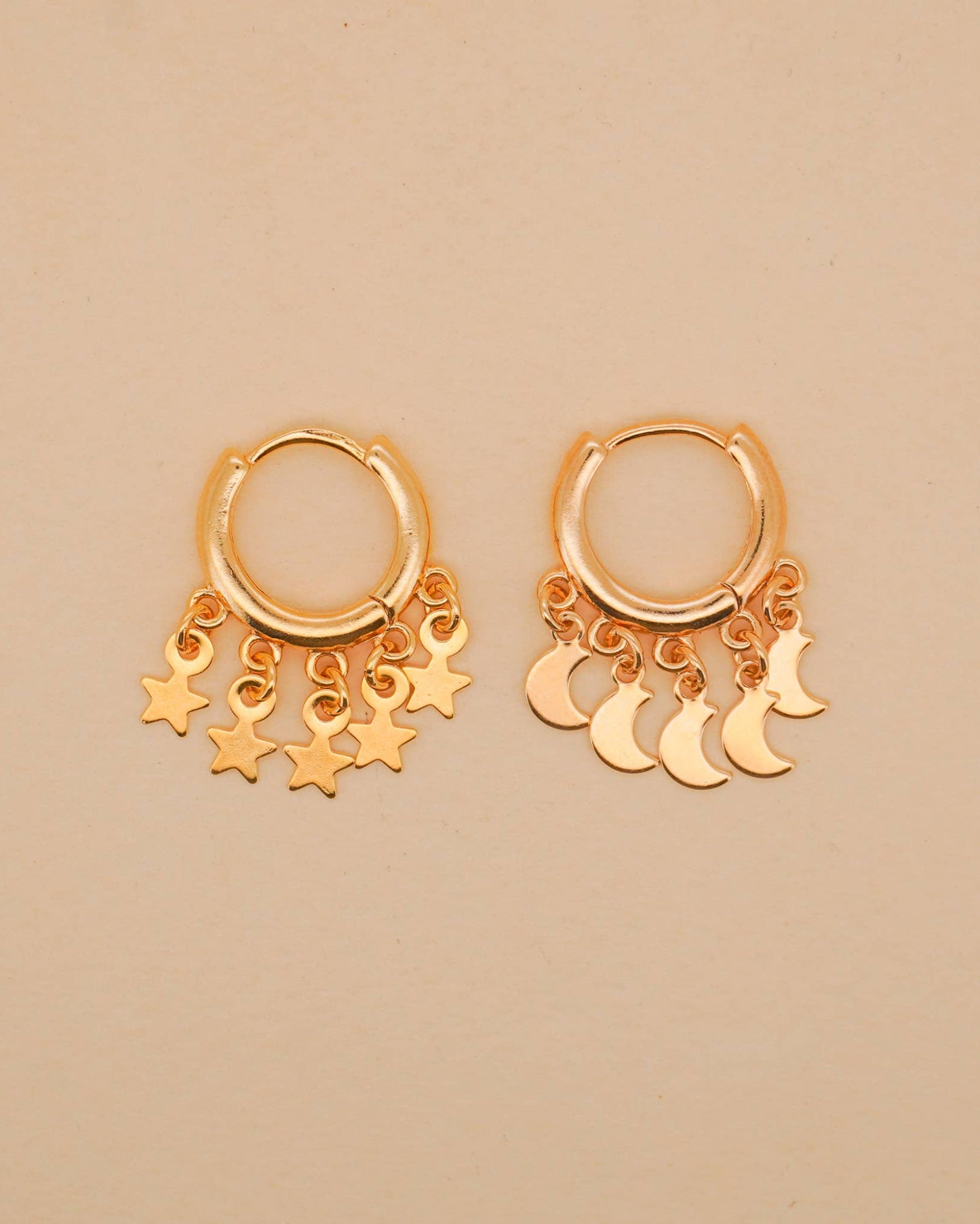 Gold hoop earrings with star and moon charms on a beige background
