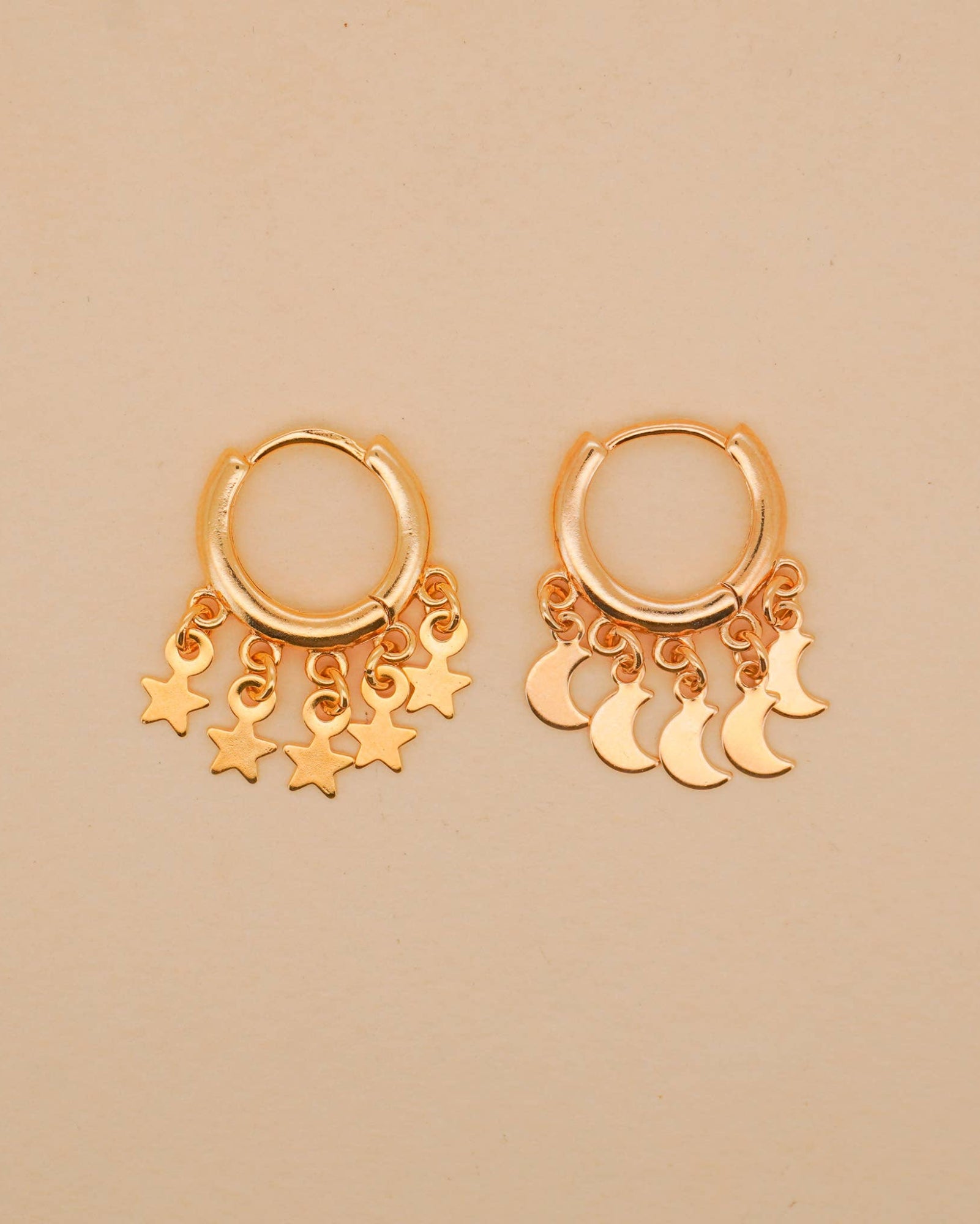 Gold hoop earrings with star and moon charms on a beige background