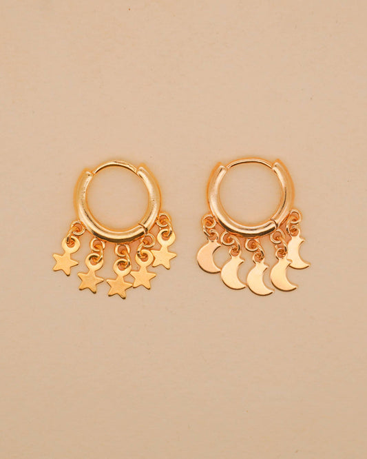 Gold hoop earrings with star and moon charms on a beige background
