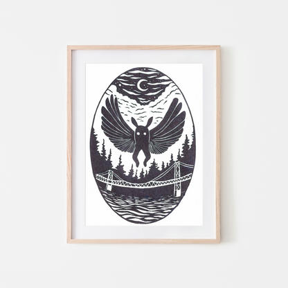 A framed art print featuring a black and white linocut-style illustration of a bird with spread wings over a forest, bridge, and water, under a crescent moon, shown in a light wood frame against a white wall.
