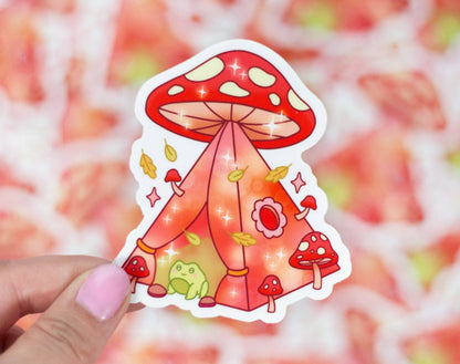 Sticker of a red mushroom with a tent-like structure held by a hand against a colorful background.