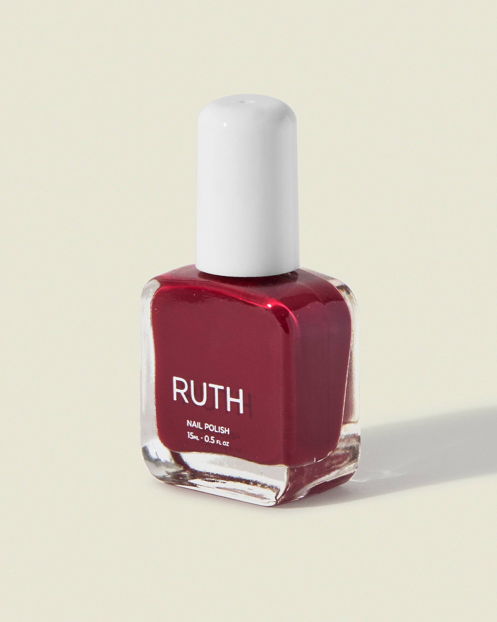 Red nail polish bottle labeled 'RUTH' on a light beige background. NYC Deep Red Nail Polish - Ruth Polish