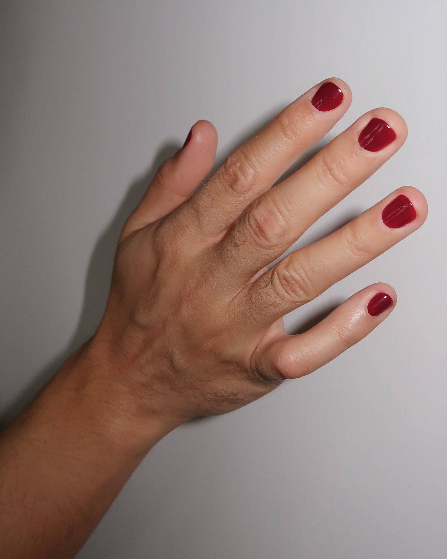 Hand with red nail polish on a plain background, NYC Deep Red Nail Polish - Ruth Polish