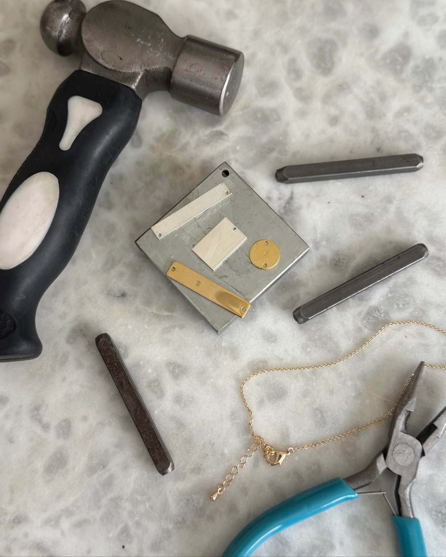 Hammer, jewelry tools, and gold necklace on a marble surface