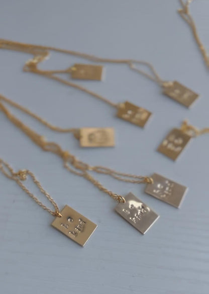 Gold necklaces with square pendants on a light blue background