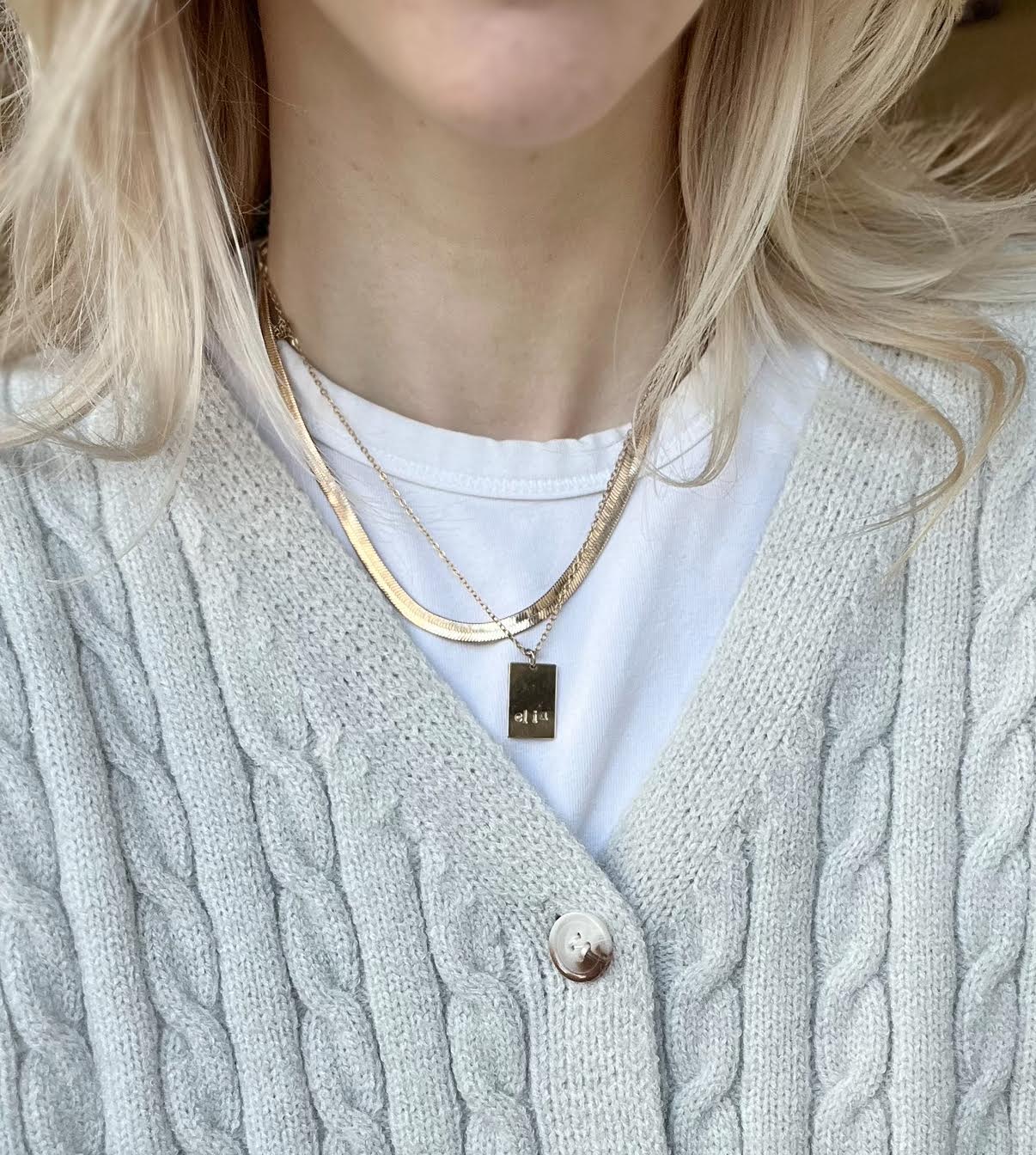 Person wearing a light gray cable knit cardigan with a white shirt and gold necklace.