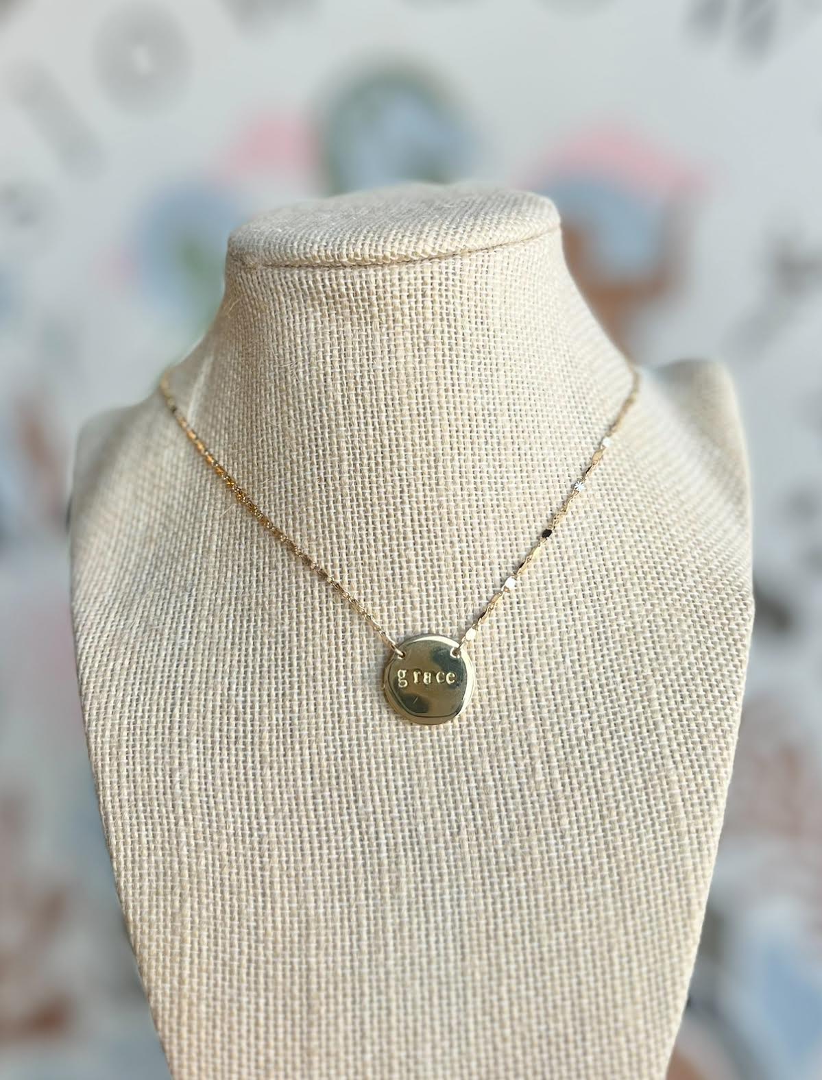 Necklace with a 'grace' pendant on a mannequin bust against a blurred background