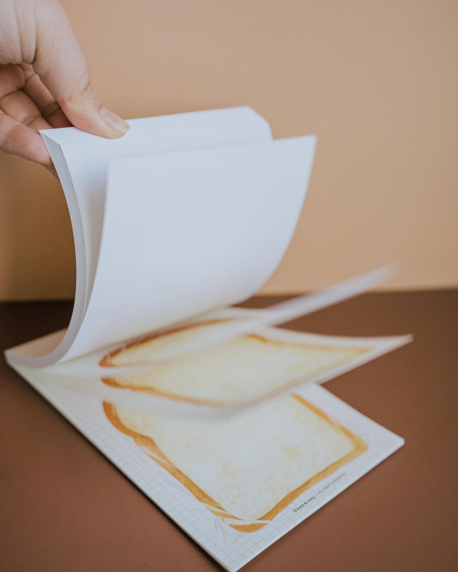 Hand holding a piece of white paper over a printed image on a brown surface