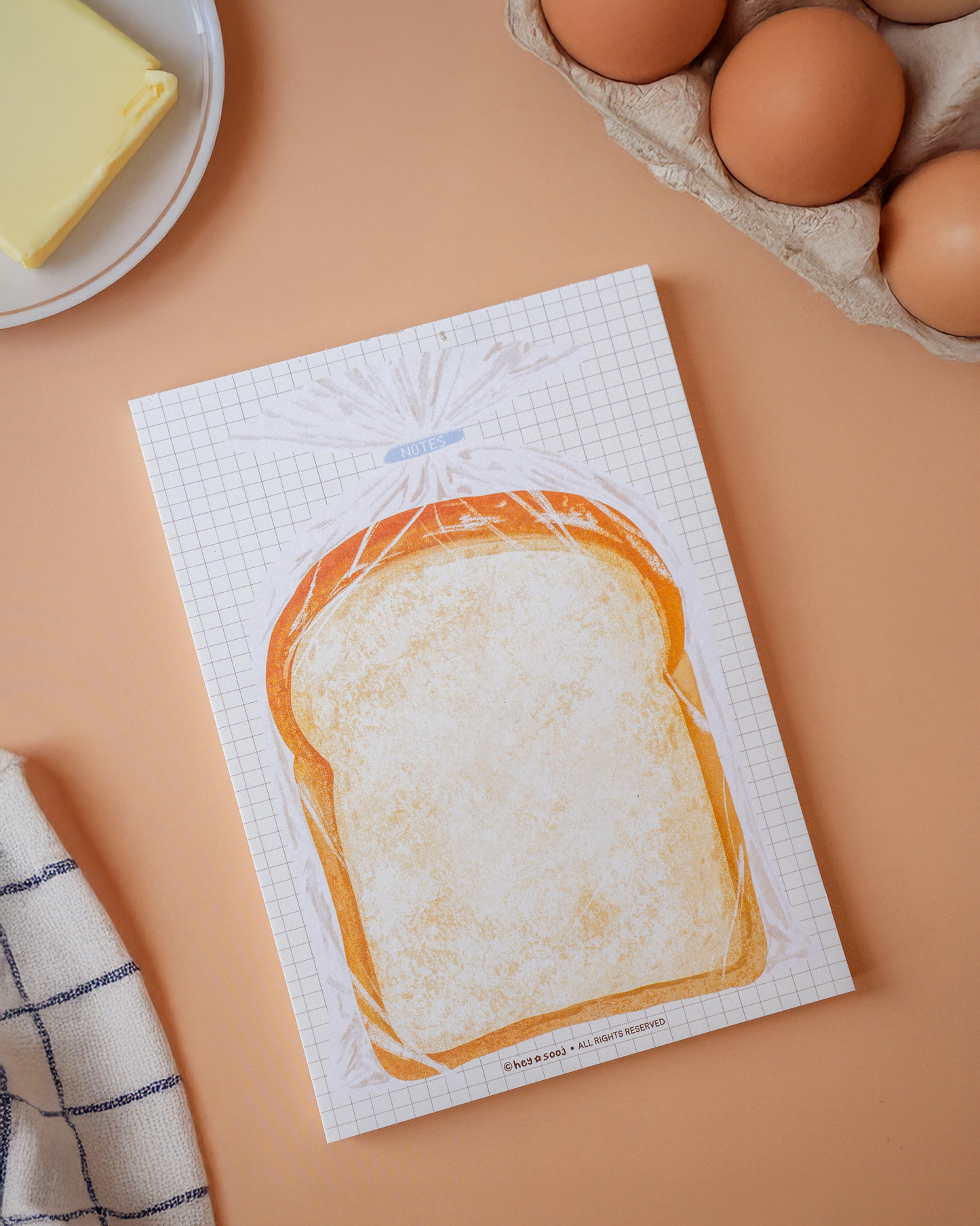 Kitchen towel with bread design on a beige surface with eggs and butter.