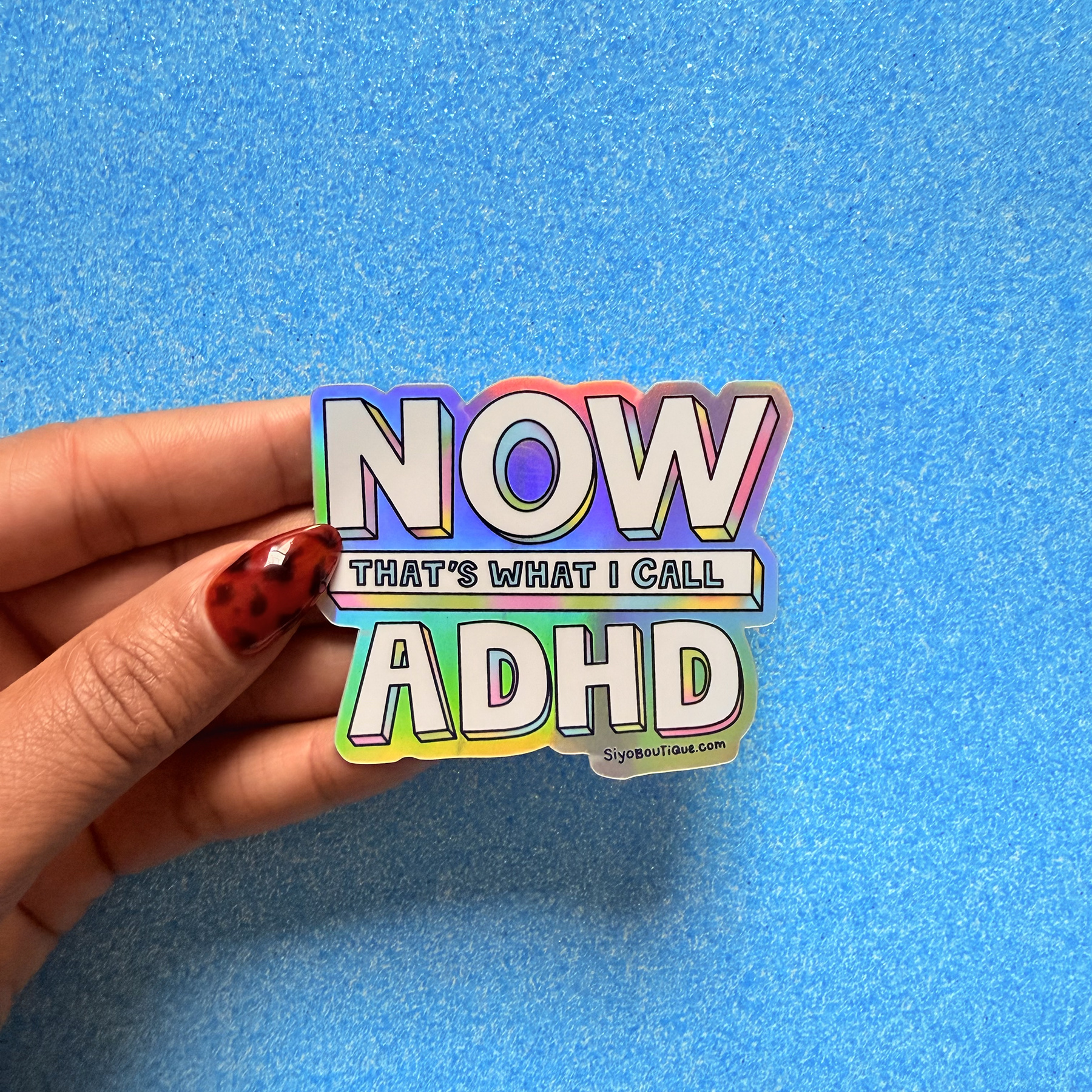 Hand holding a colorful sticker with 'NOW THAT'S WHAT I CALL ADHD' text on a blue background. Now Thats What I Call ADHD Holographic Sticker