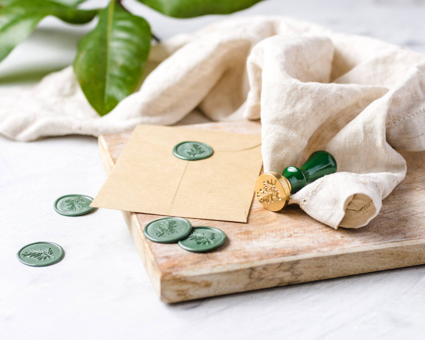 Envelopes with green stamps on a wooden board with a white cloth and plant leaves in the background