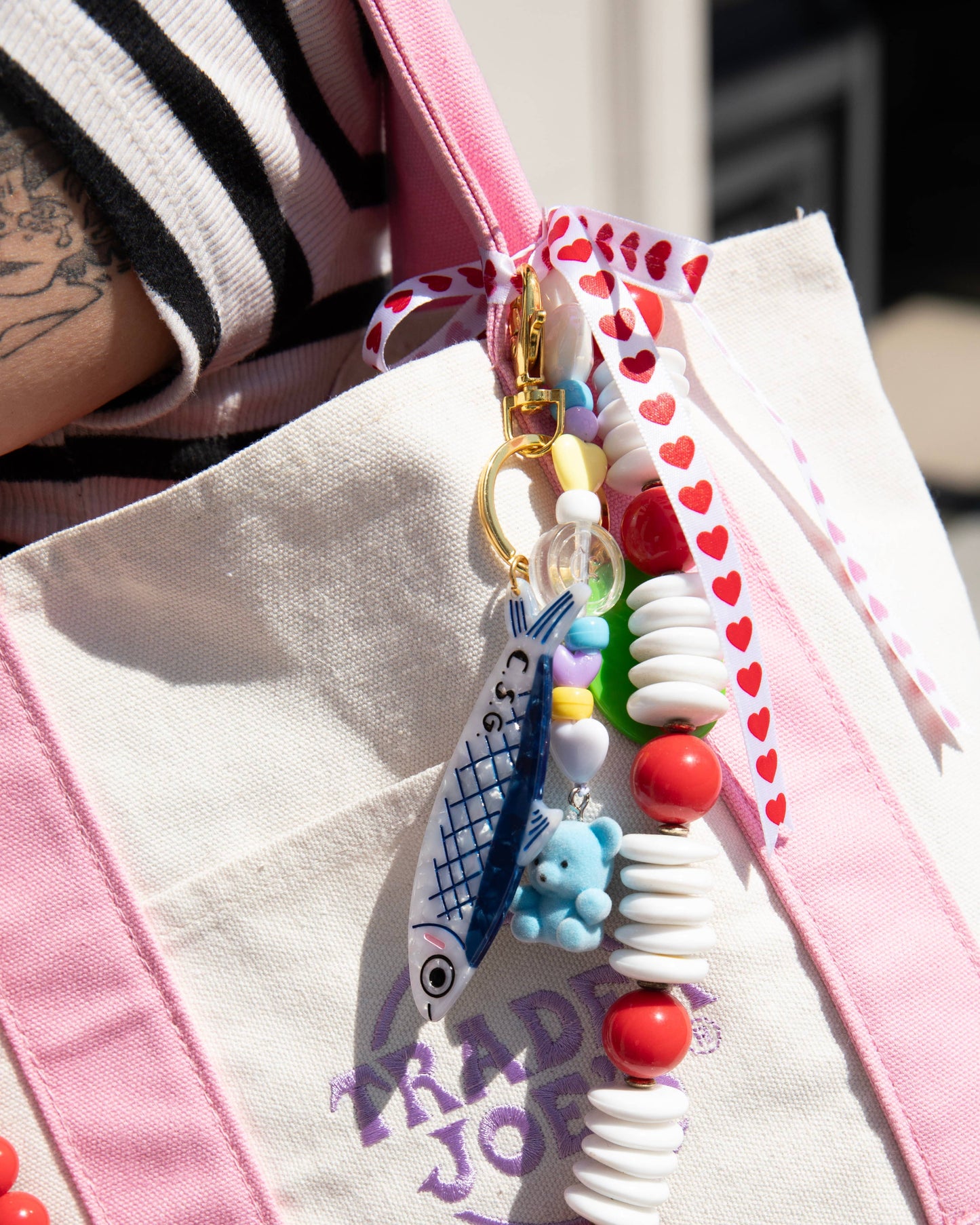 Colorful beaded keychain attached to a pink and white bag with text.
