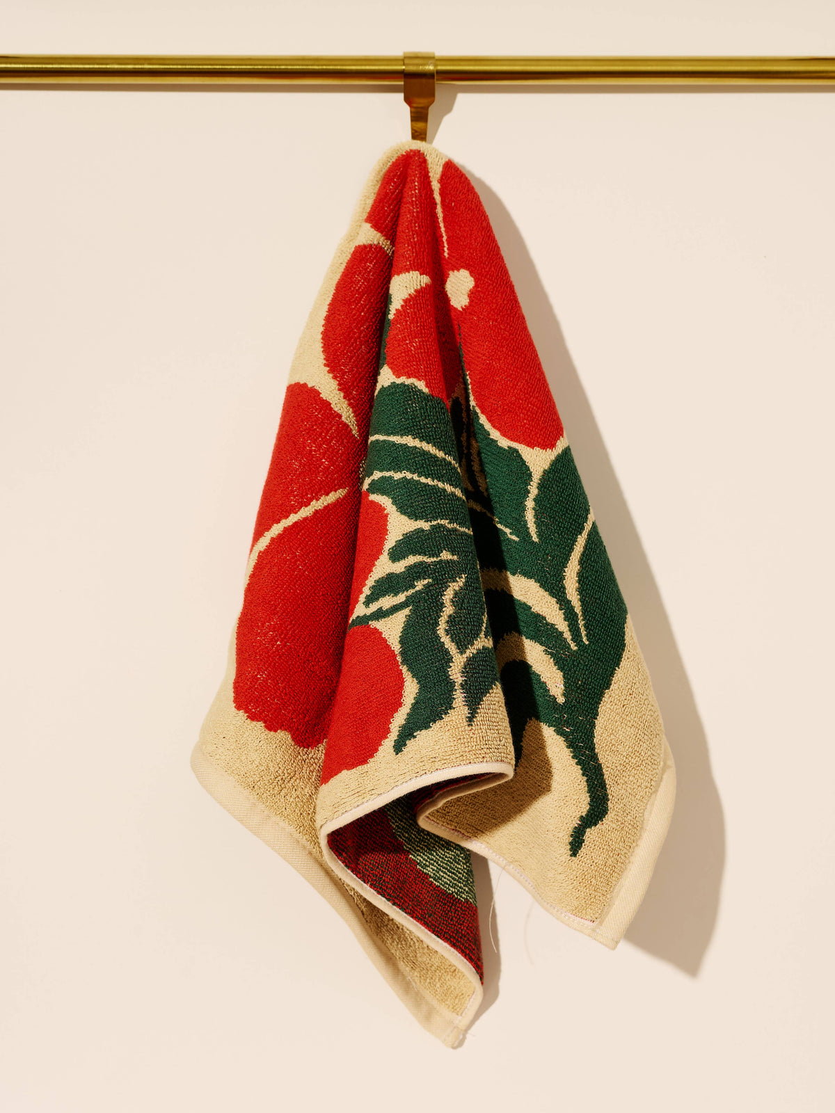 Woven towel with red and green design hanging on a gold rod against a beige background