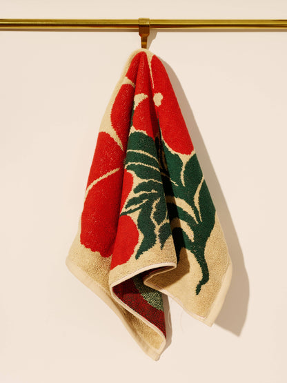 Woven towel with red and green design hanging on a gold rod against a beige background