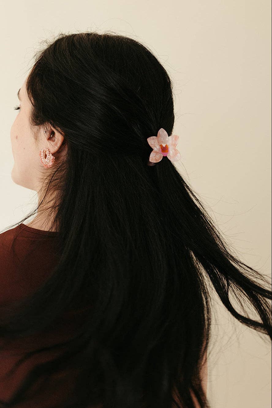Woman with long dark hair wearing a floral hair clip against a neutral background