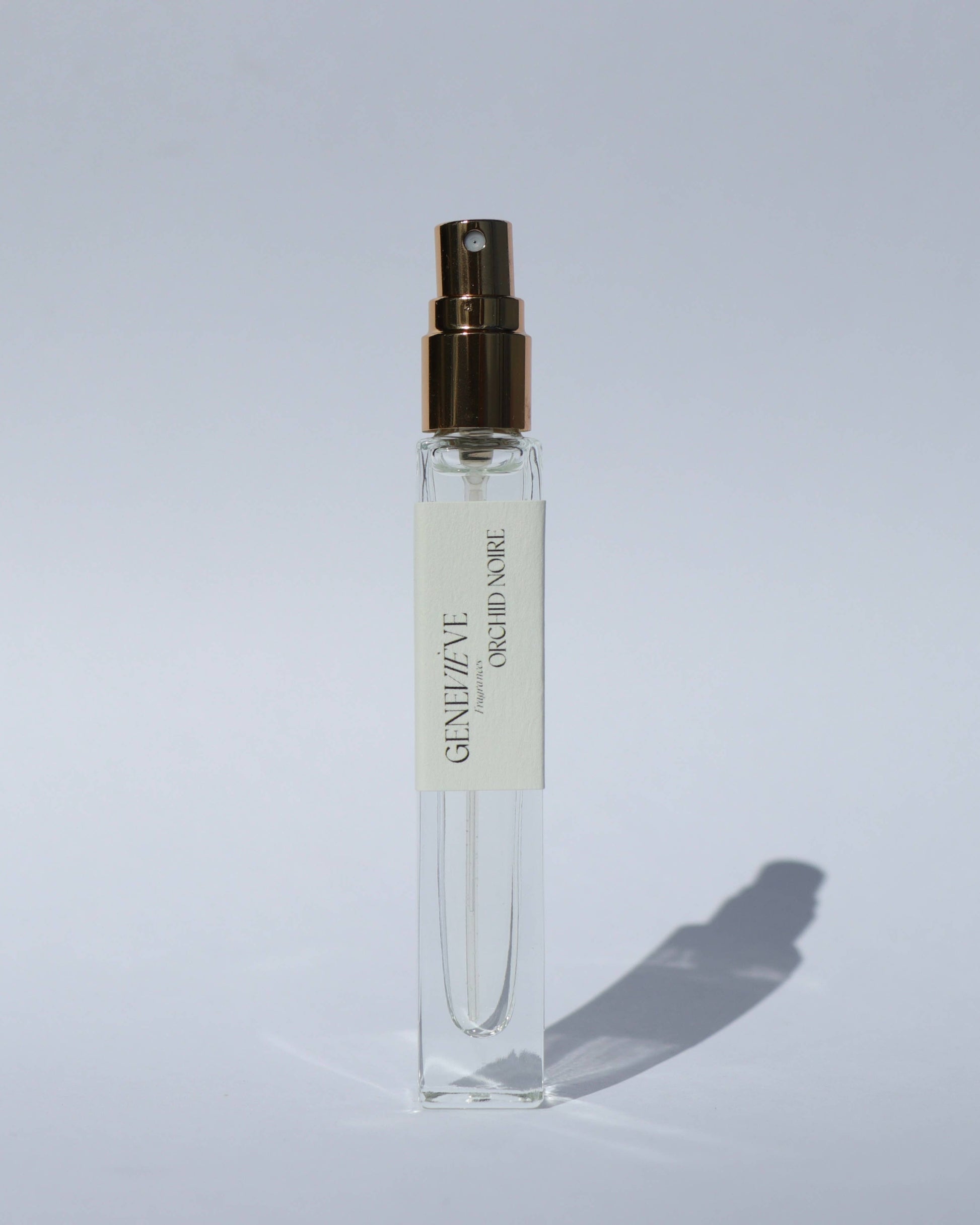 Small clear spray bottle with gold cap on a light gray background