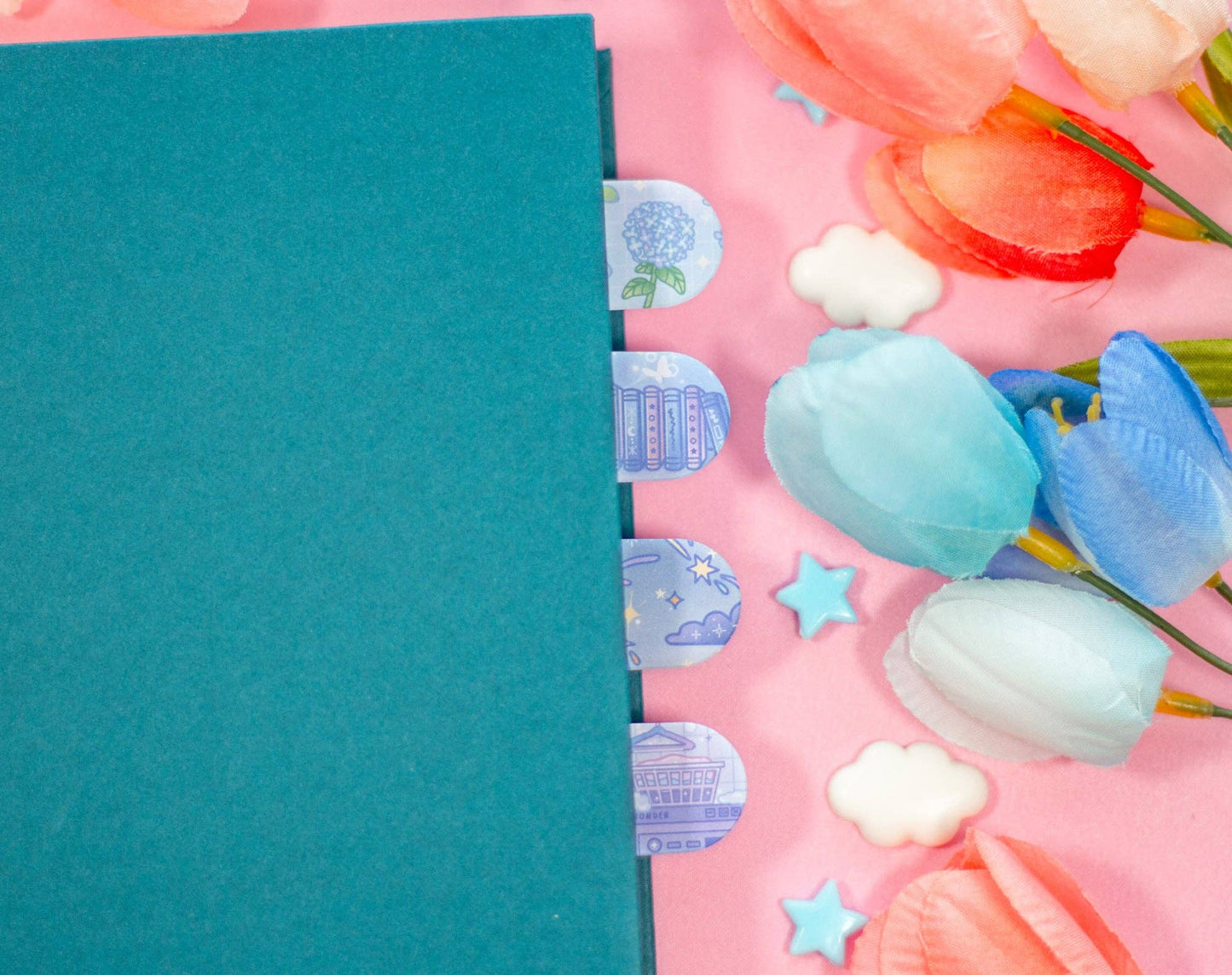 Teal notebook with decorative stickers on a pink background with tulips