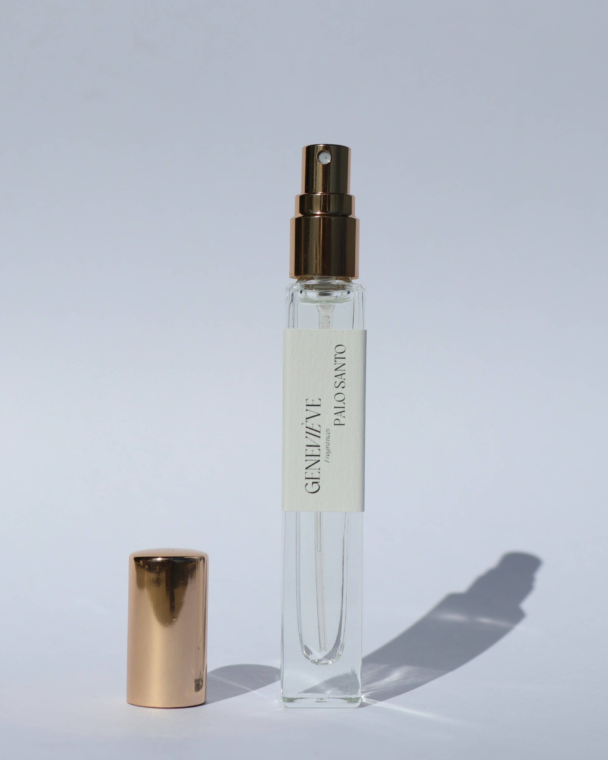 Clear spray bottle with gold cap on a light gray background