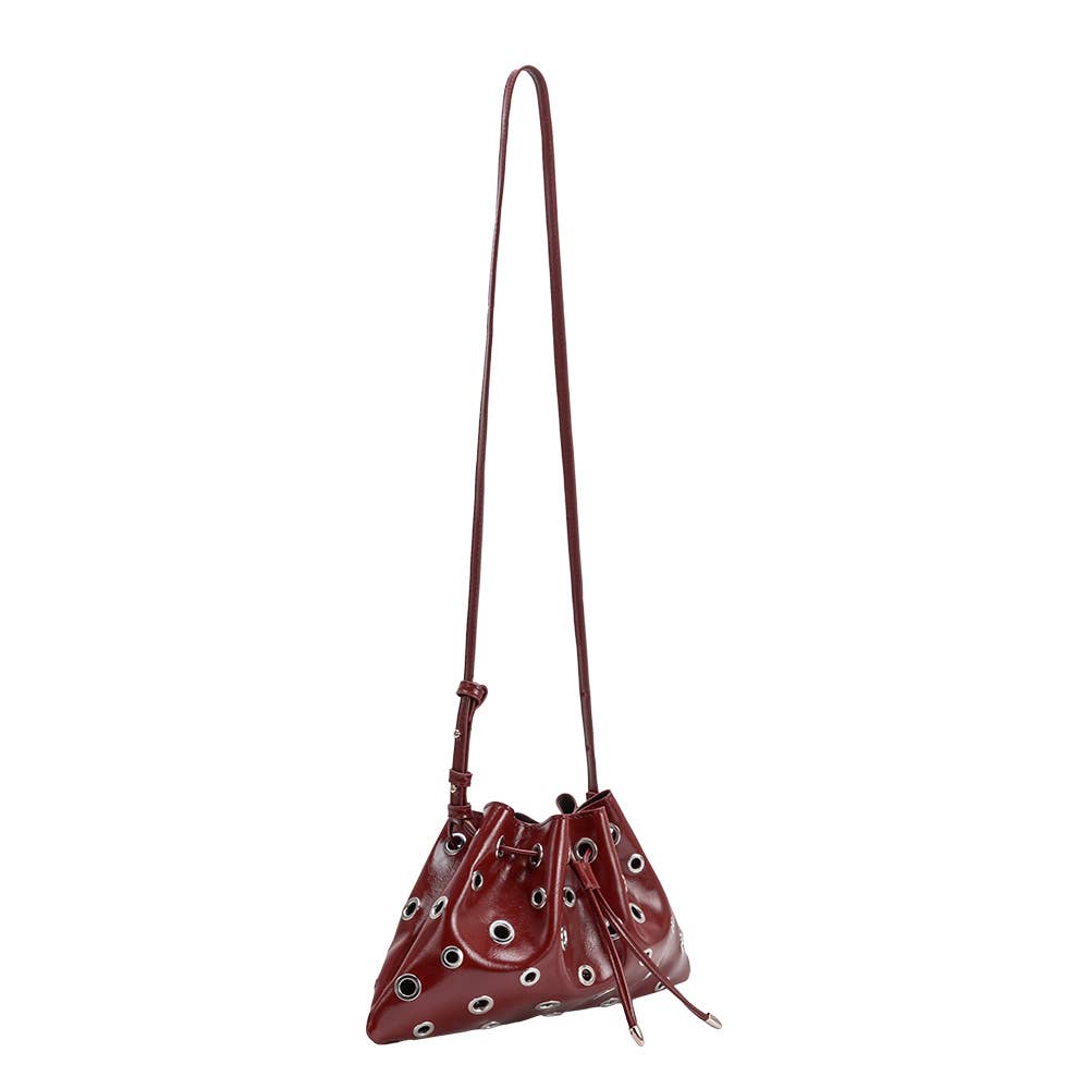 A glossy burgundy leather bucket bag with silver-tone grommets and a long shoulder strap, shown against a plain white background.