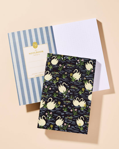 Two notebooks, one with blue stripes and the other with a swan pattern, on a beige background.