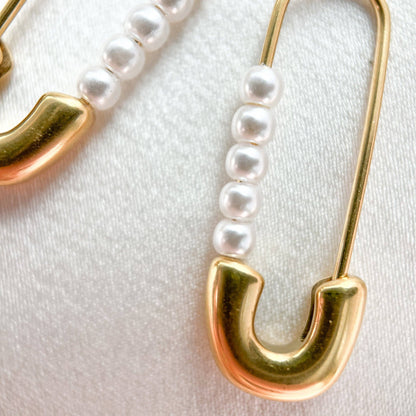 Gold safety pin earrings with pearl beads on a white background