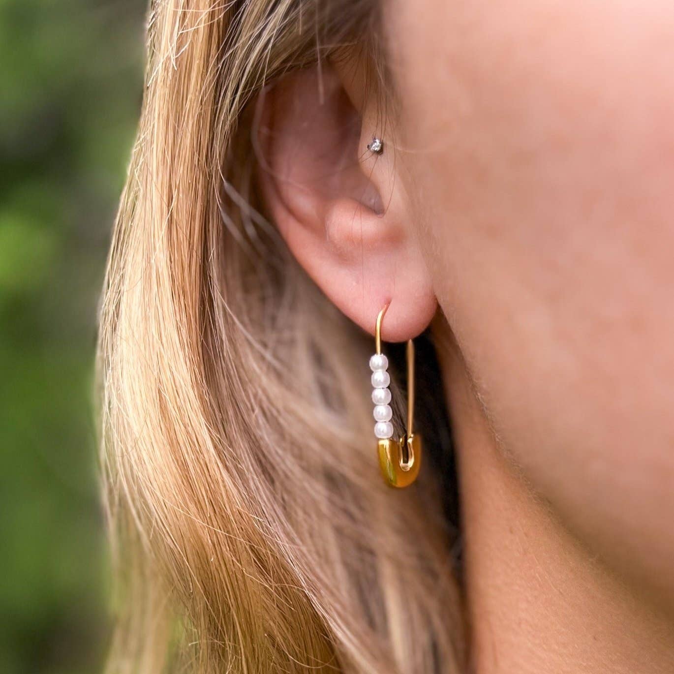 Close-up of an ear wearing a gold earring with pearls against a blurred natural background