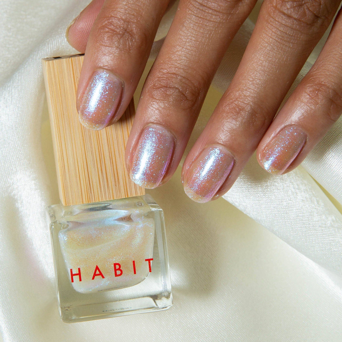 Hand with glittery nails holding a bottle of 'Habit' nail polish.