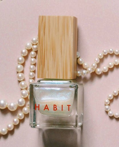 Nail polish bottle with wooden cap and 'Habit' branding on a pink background with pearls.