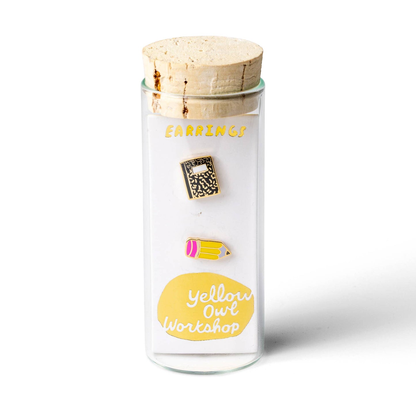 A pair of enamel pins shaped like a notebook and a pencil, displayed on a white card inside a clear glass jar with a cork lid. The card features the text 'EARRINGS' and 'Yellow Owl Workshop'.