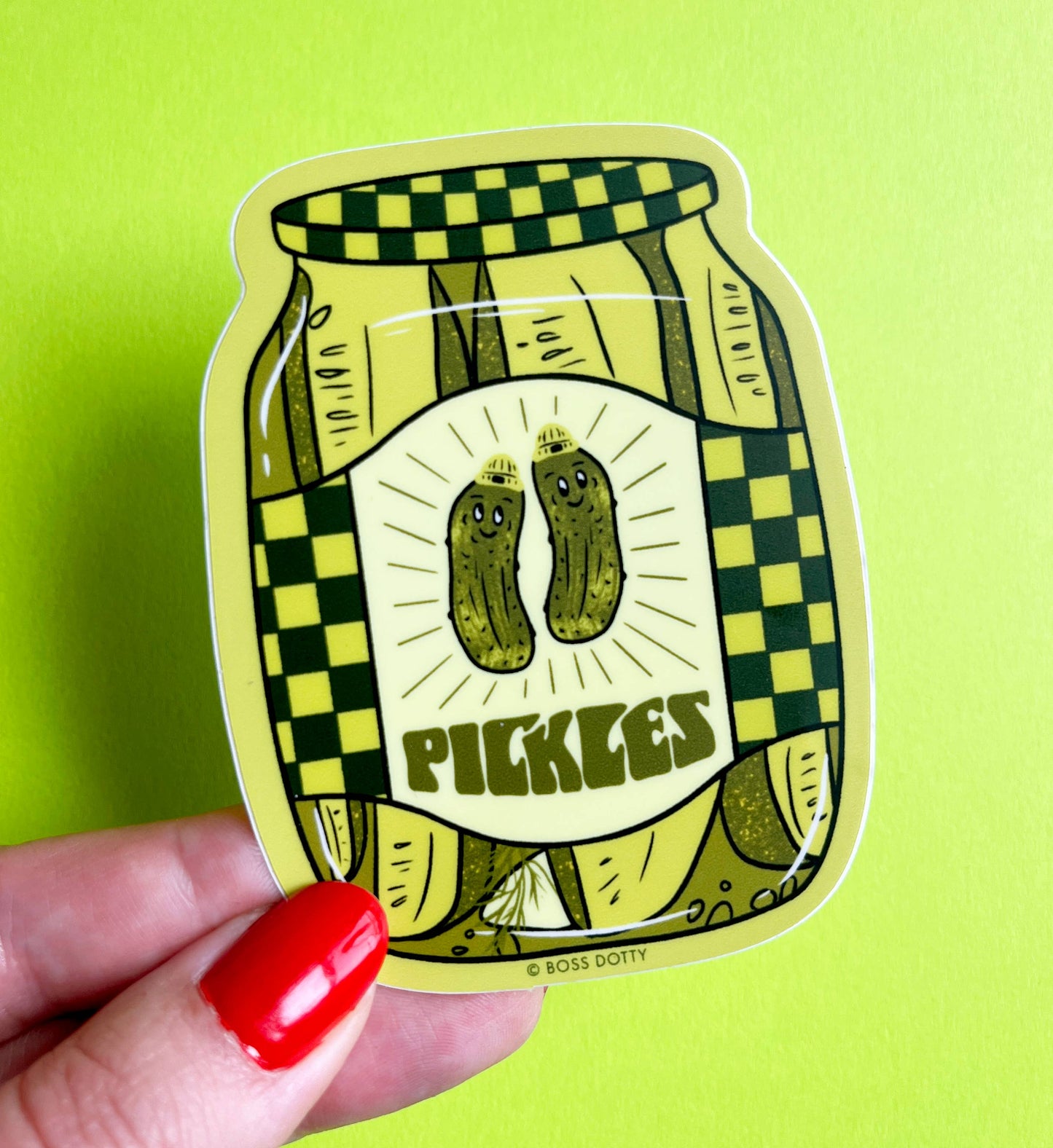 Sticker of a jar of pickles held by a hand with red nail polish on a green background