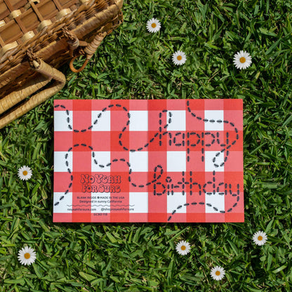 Red and white checkered birthday card on grass with flowers