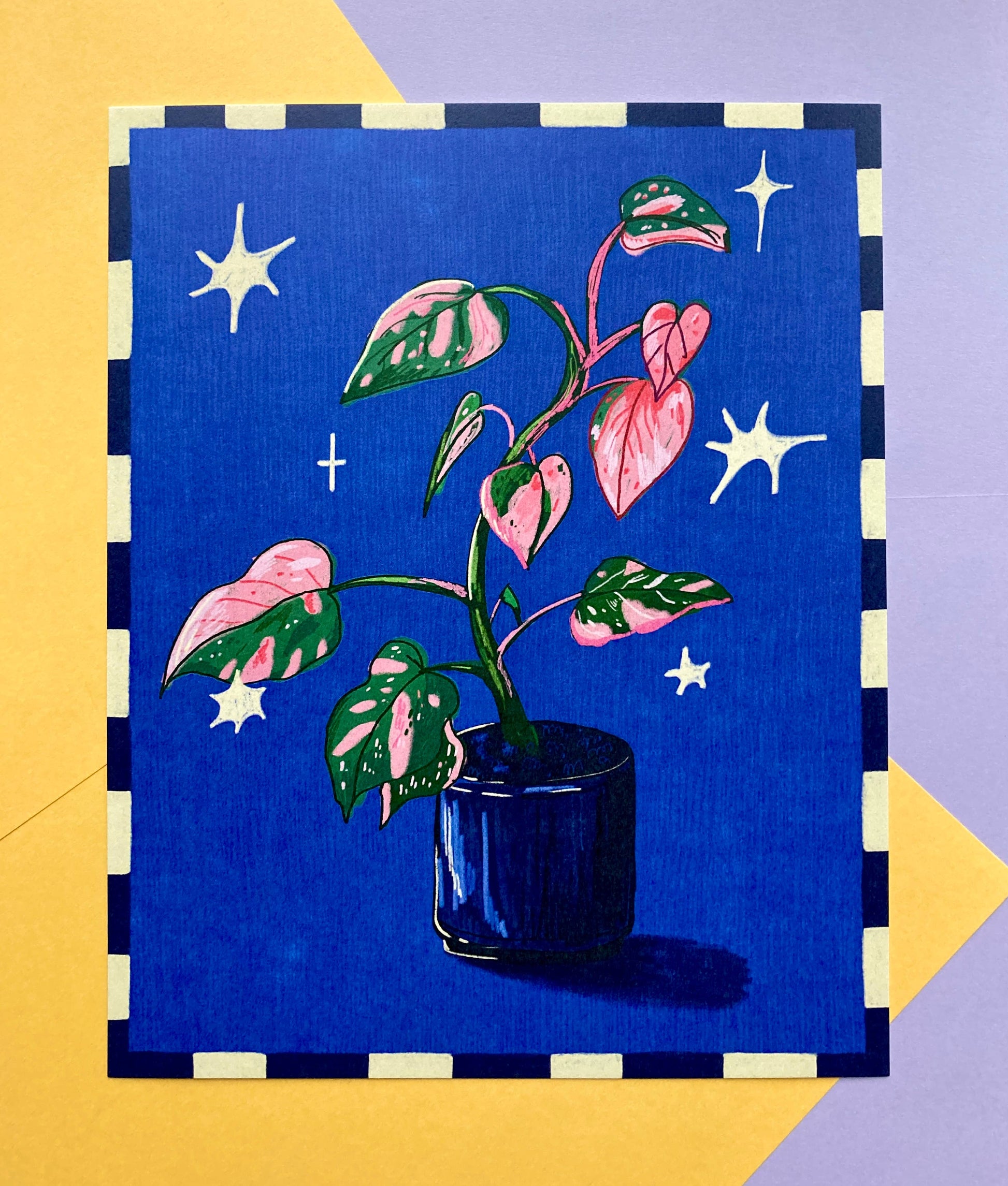 A square art print or card featuring a stylized illustration of a potted plant with pink and green variegated leaves on a deep blue background with white stars, bordered by a black and cream check pattern, set against a yellow and lavender background.