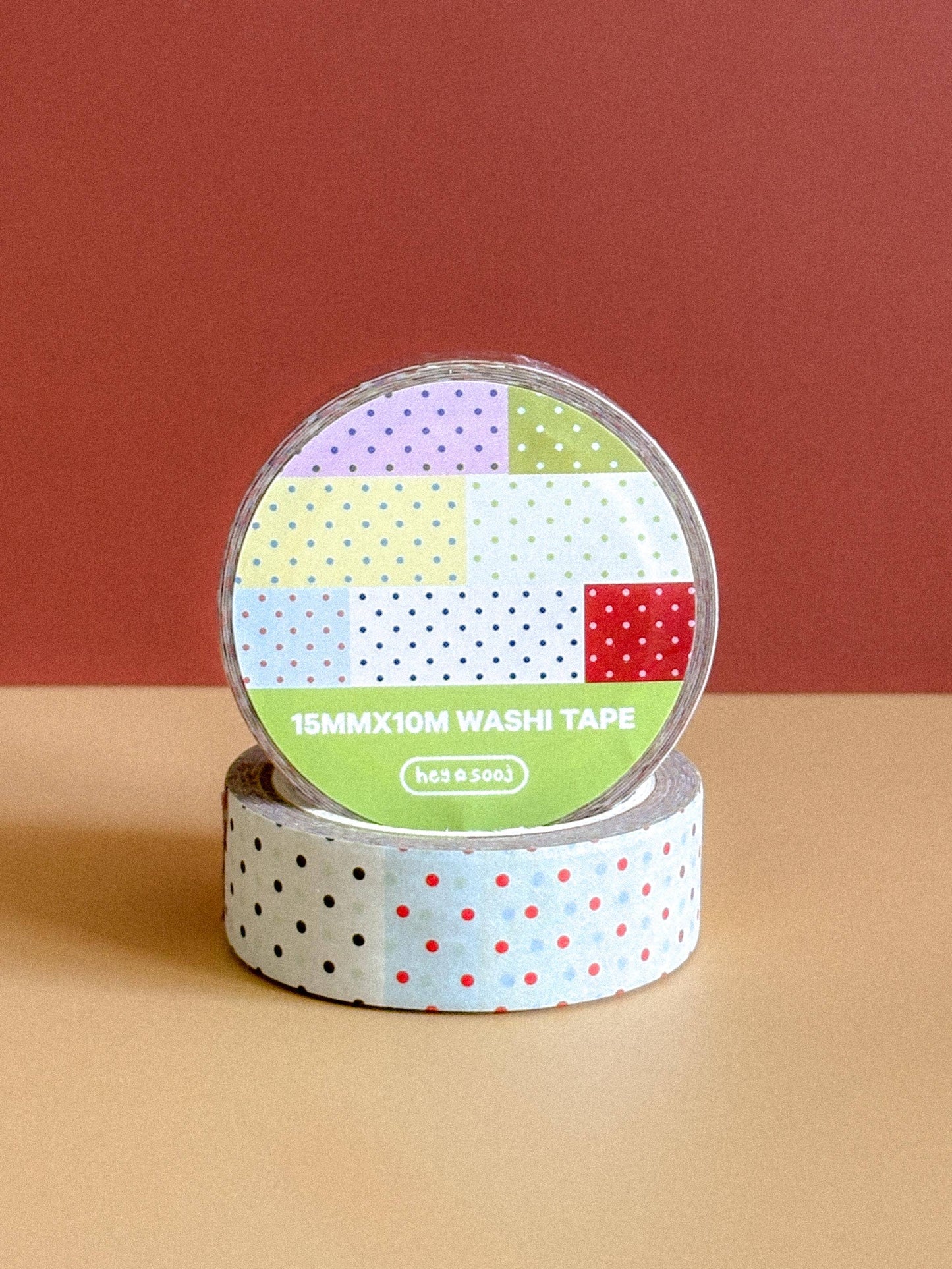 Two rolls of washi tape with colorful patterns on a beige surface and red background