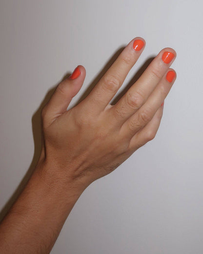 Hand with orange nail polish on a plain background, ruth nail polish