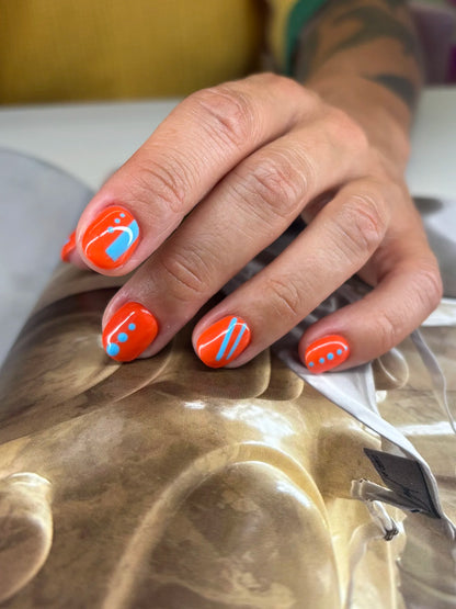 Hand with orange nail polish and blue patterns on a textured surface