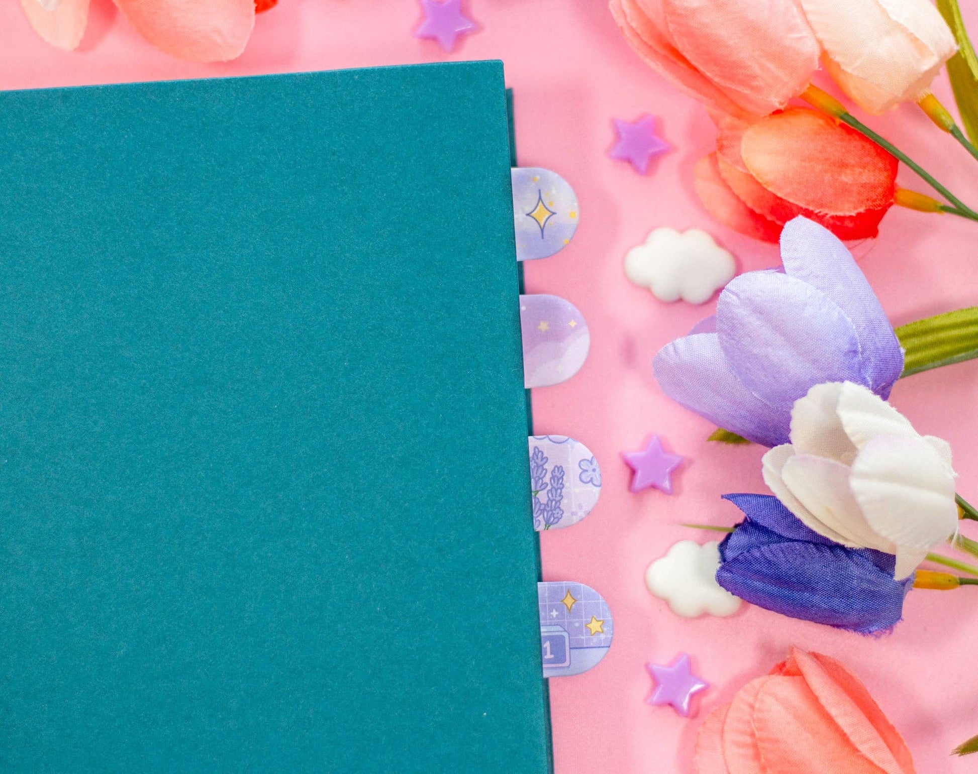 Teal notebook on a pink background with decorative flowers and stars
