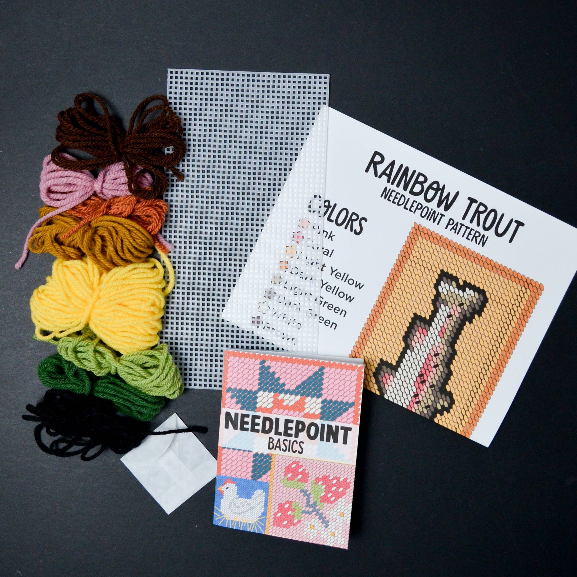 Needlepoint kit with yarn, grid paper, pattern sheet, and book on a dark surface