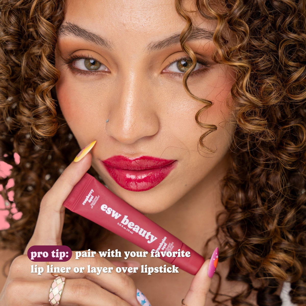 Woman holding a pink lipstick with 'esw beauty' branding, wearing bright pink lipstick.