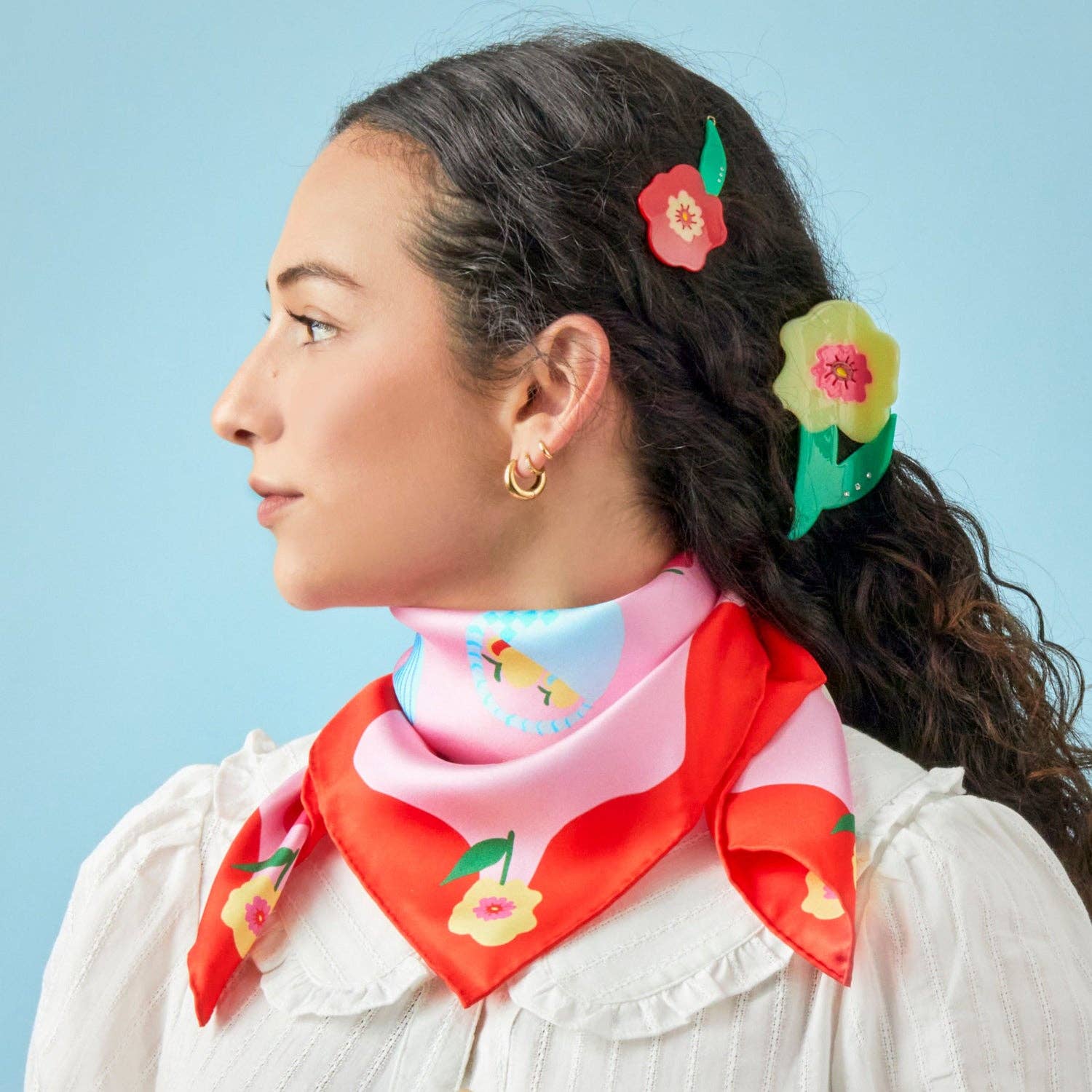 Woman wearing a colorful scarf and floral hair accessories against a light blue background