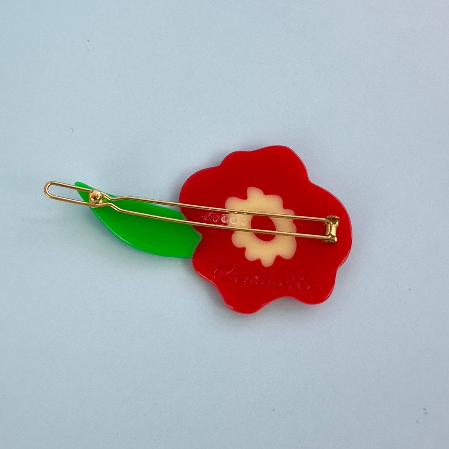 Red flower-shaped brooch with gold and green accents on a light blue background, Red Flower Hair Clip