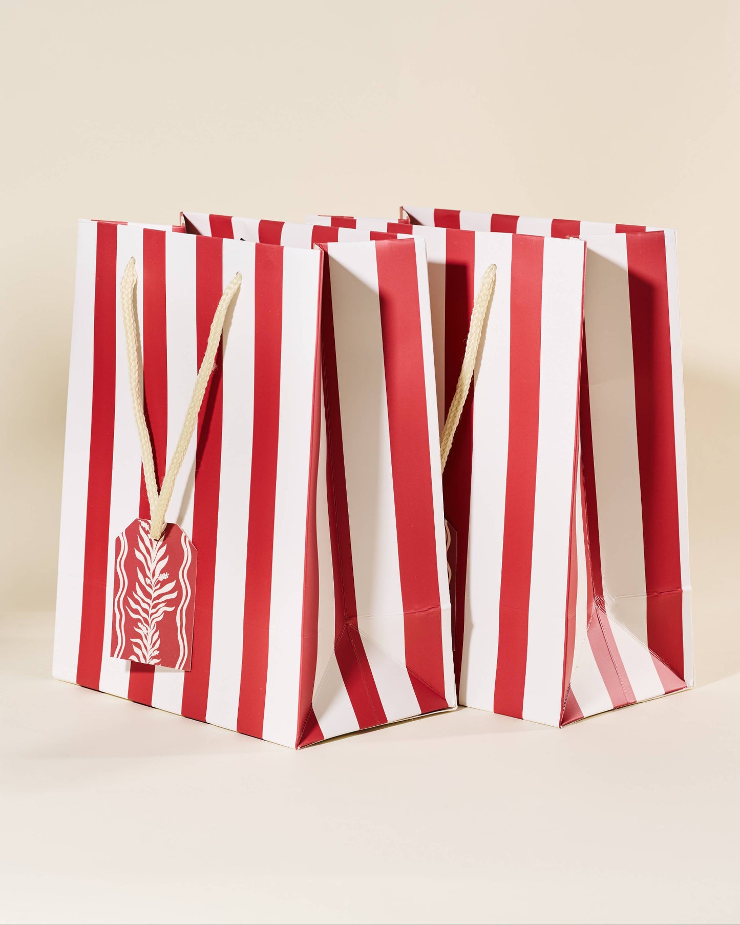 Two red and white striped bags with wooden sticks on a beige background